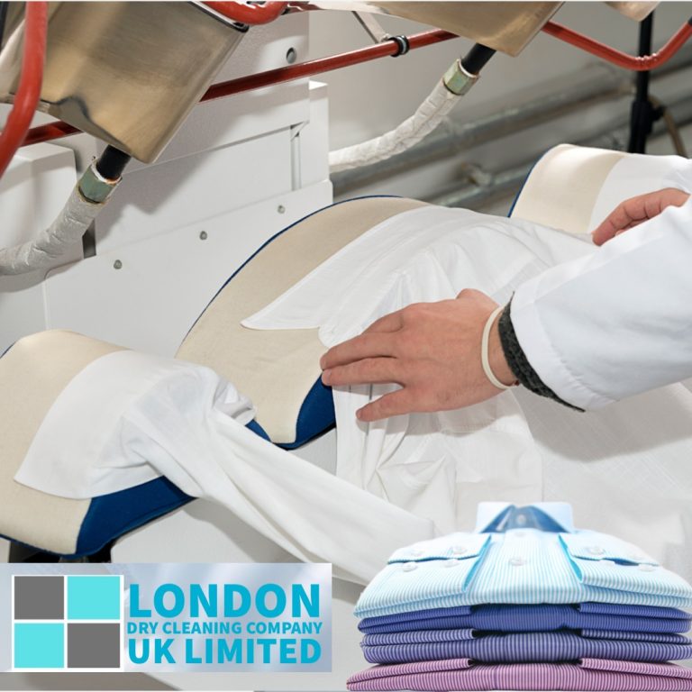 A person uses a pressing machine to iron a white shirt. The machine has padded components. A stack of folded shirts, ready for the Christmas season, is visible at the bottom right. The logo of London Dry Cleaning Company UK Limited is in the bottom left corner.