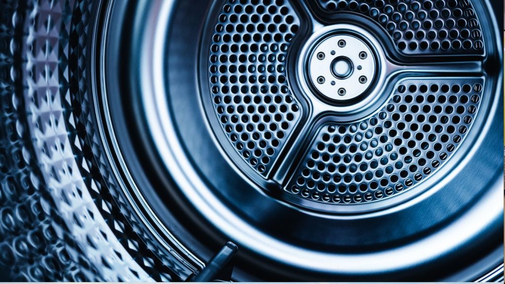 Close-up view of the interior of a washing machine drum with a metallic blue hue. The perforated circular surface and geometric patterns mirror the meticulous standards found in top London dry cleaning services, highlighting the machine's design and texture.